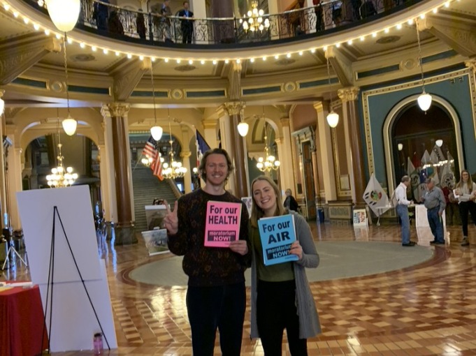 Guy and Girl standing in main hall of building with For our Health/ Air papers
