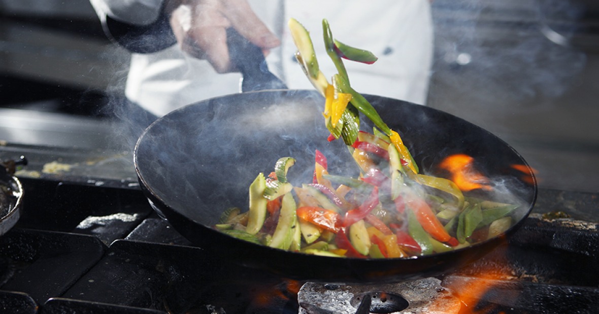 Vegetables being tossed in a skillet over a flame on a stove